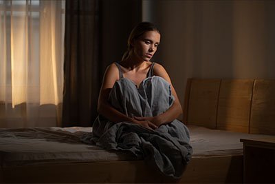 Бессонница Женщина сидит в кровати и обнимает колени