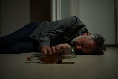 Запойное состояние Мужчина лежит на полу и тянется к бутылки